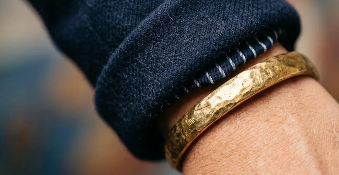Dettaglio ravvicinato di manica blazer arrotolata con bracciale dorato che la fissa